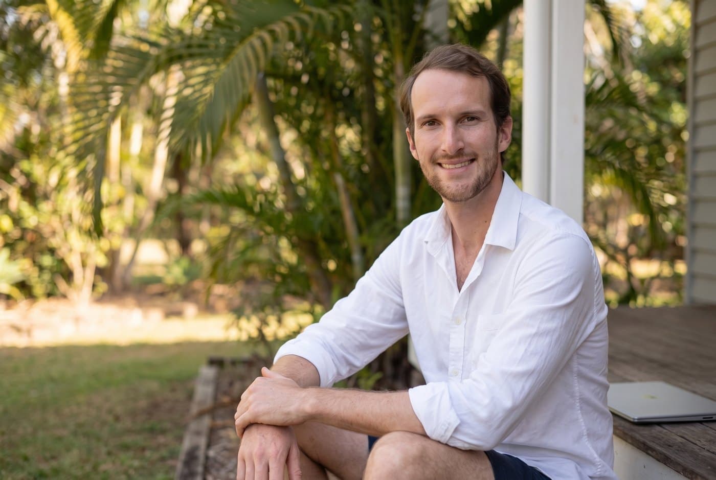 Peter Low sitting on a timber verandah in a leafy garden